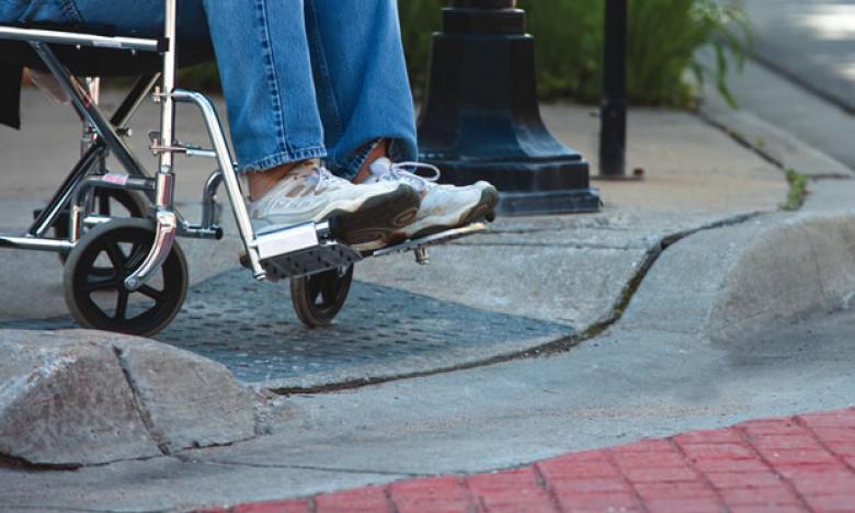 Low shot of a person in a wheelchair preparing to roll through a curb cut.