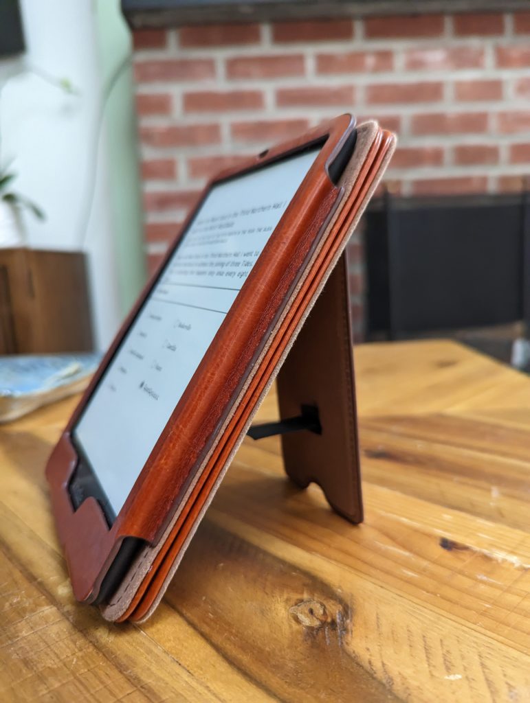 Kindle Paperwhite in a brown case with a stand on a wooden table. 
