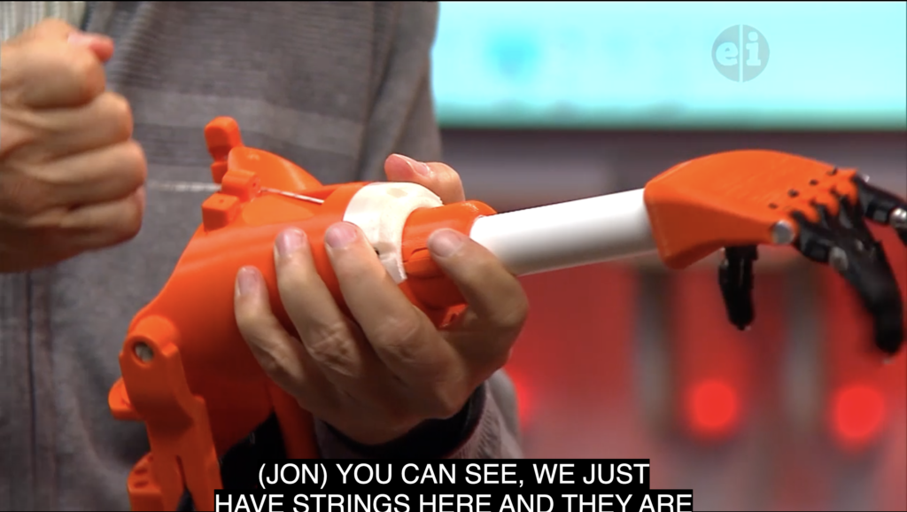 Image of scientist holding white and orange 3-D printed prosthetic arm. 