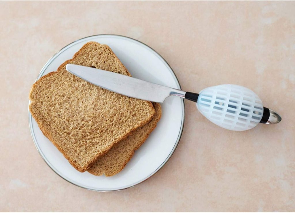 Image of a knife inside of NuMuv Grip-Aid. One end of the knife is placed on top of two pieces of toast. The toast is on a white plate.