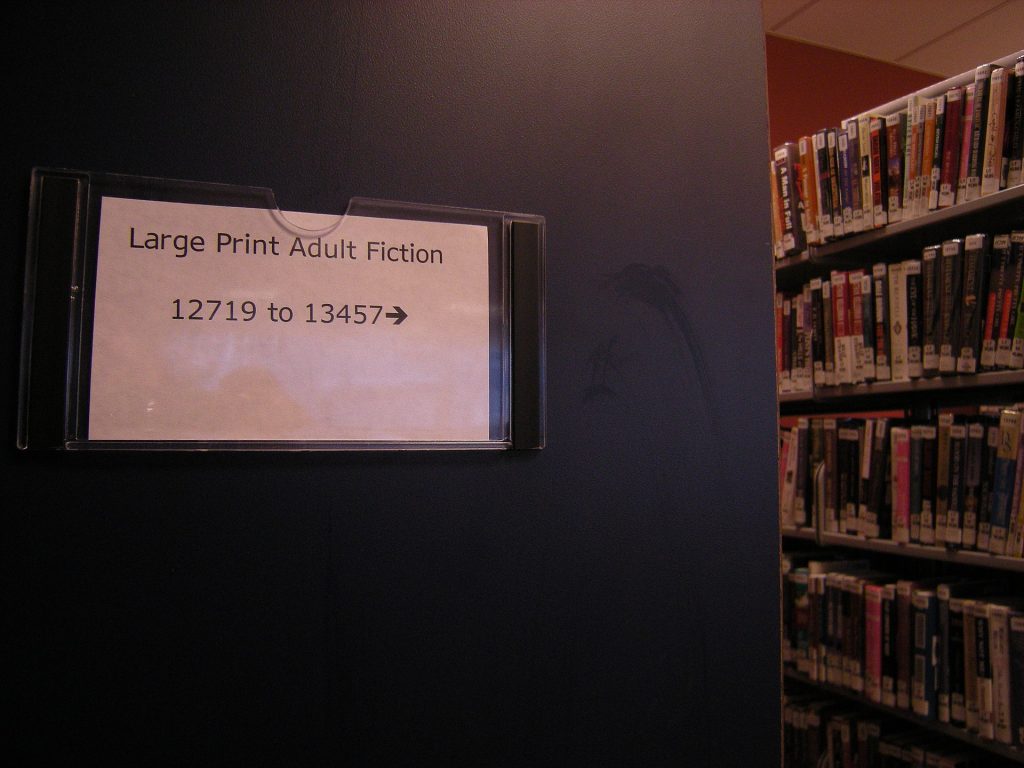 Sign in a library pointing to adult fiction large print collections